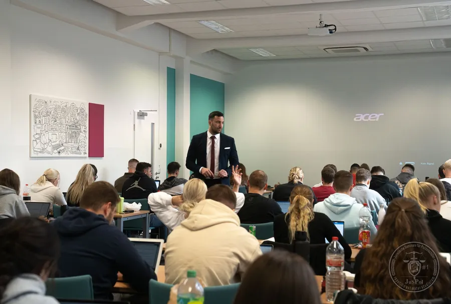 Ein Mann im Anzug hält vor einer Gruppe von Studenten in einem Hörsaal eine Präsentation.