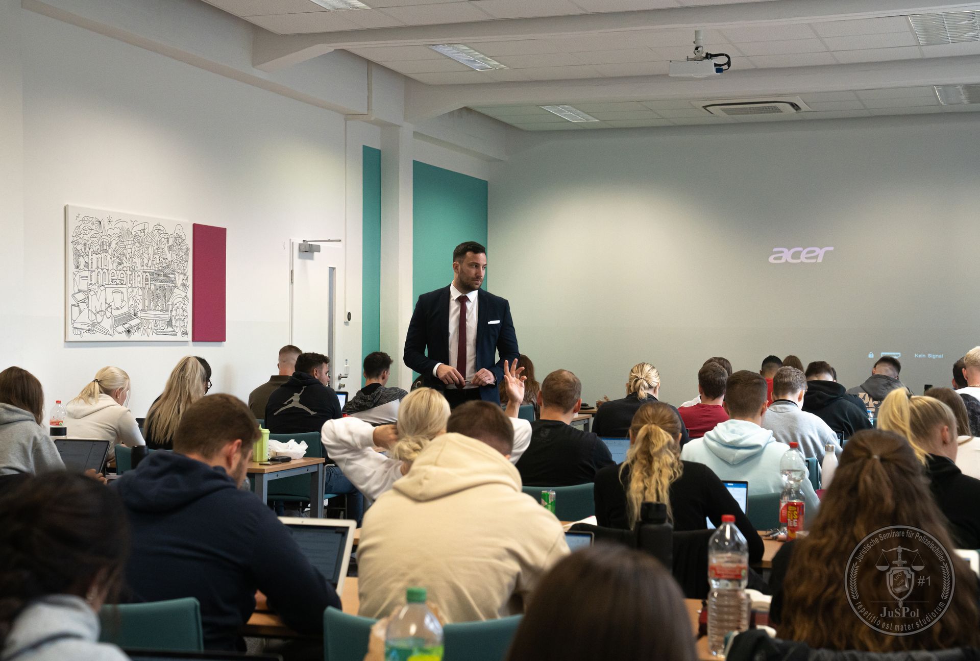 Ein Mann im Anzug hält vor einer Gruppe von Studenten in einem Hörsaal eine Präsentation.